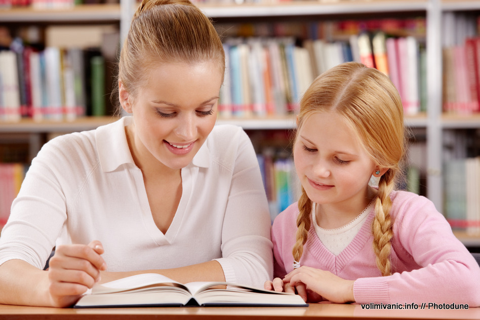 Portrait of schoolgirl and teacher reading interesting book in library