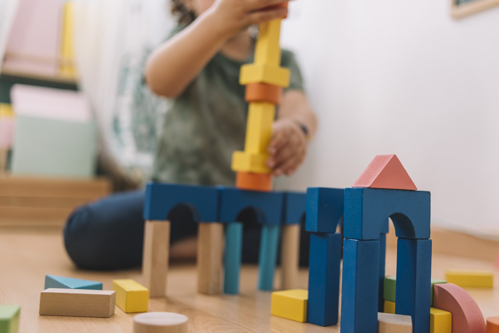 colorful wooden building blocks with a little girl unfocused in the background playing happy in the floor at home or kindergarten, educational toys for creative children