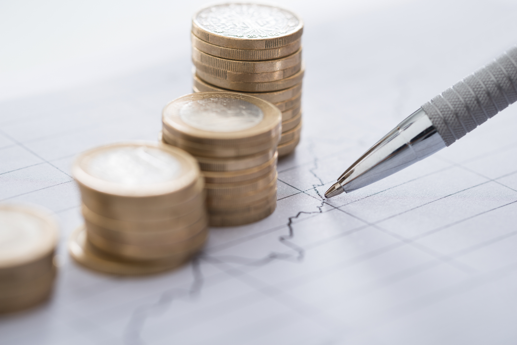 Cropped image of businessman's hand with pen analyzing line and coins graphs on desk